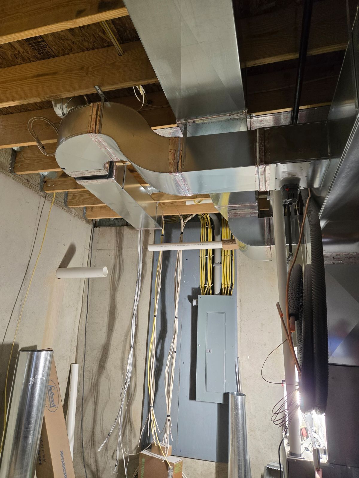 Exposed ceiling ductwork and electrical panels in an unfinished basement utility room