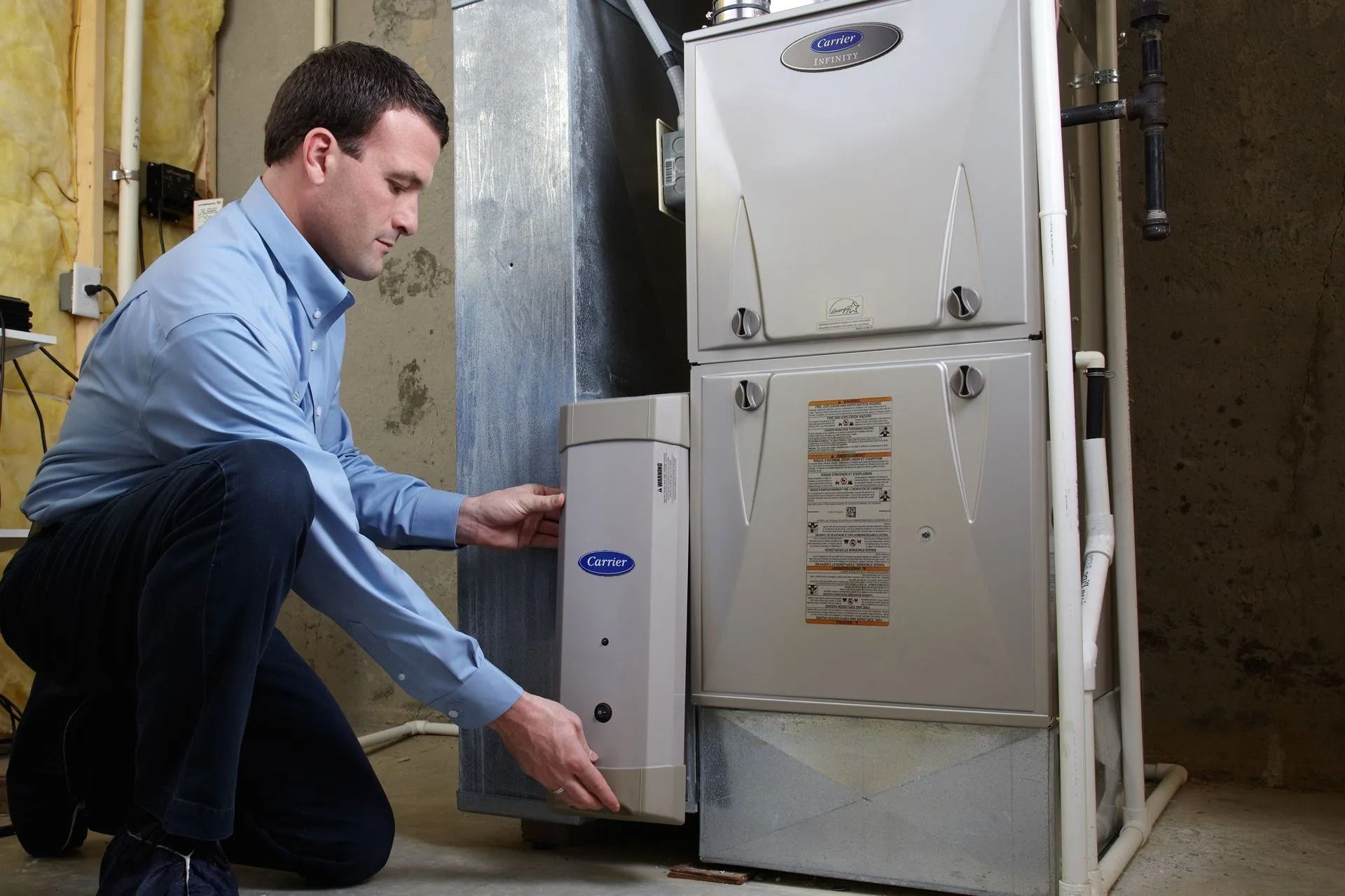 Man inspecting furnace, kneeling near a heating system in a basement.