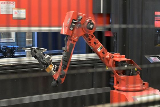 Red robotic arm in a factory, holding metal piece