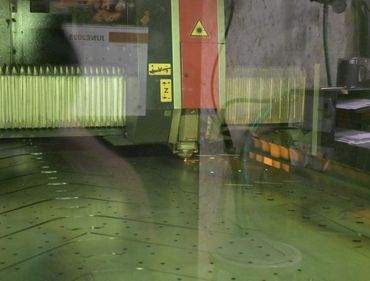 Laser cutter in operation, with yellow laser beam and metallic work surface