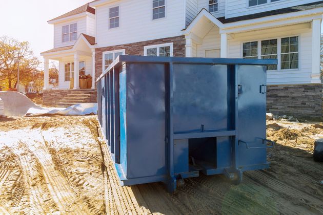 Blue dumpster in front of a house on a snowy driveway