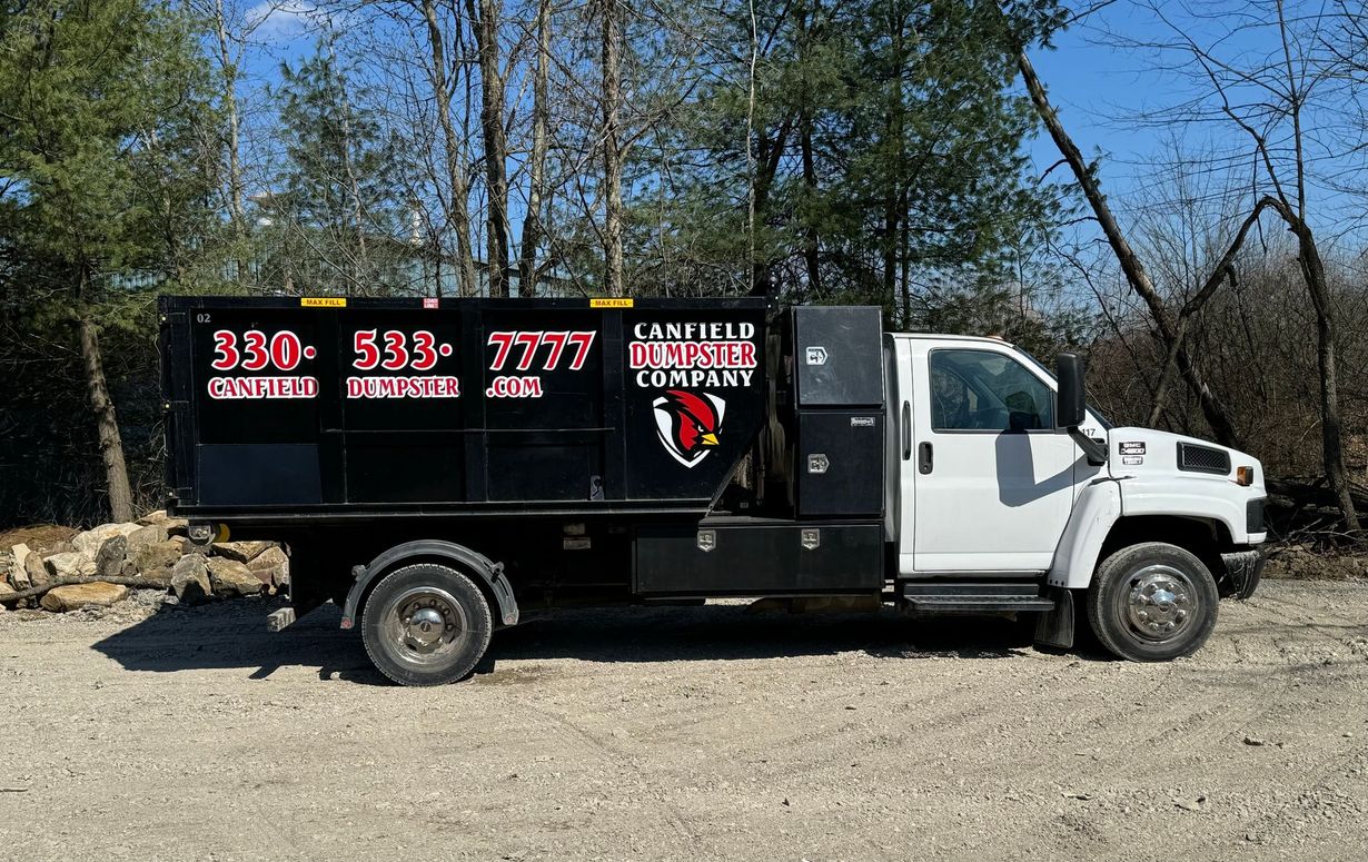 White truck with black signboard parked on gravel in a wooded area