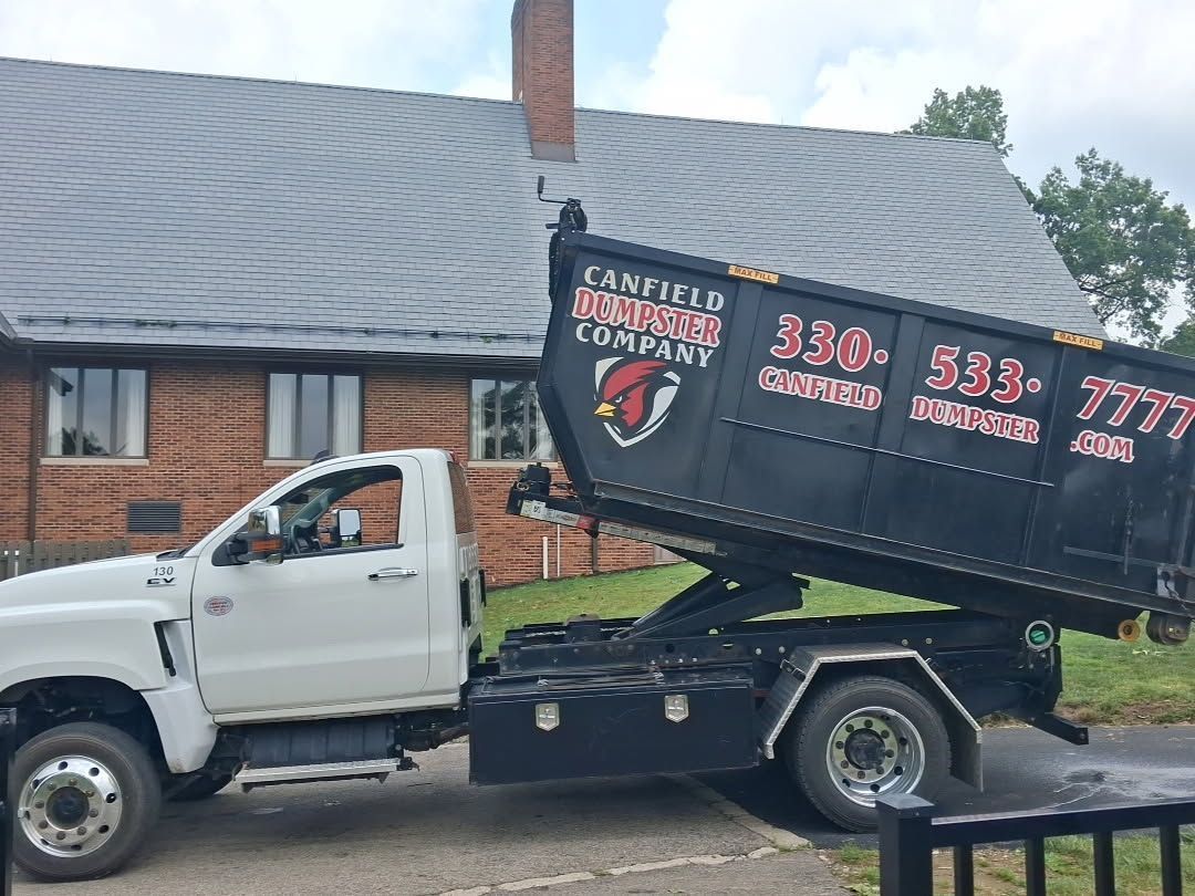 White dump truck with a raised black bed parked beside a brick building under a cloudy sky.