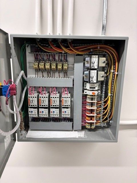 Open electrical control panel with wiring, relays, and circuit breakers in a gray cabinet