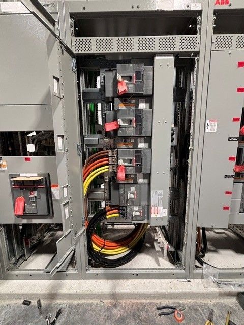 Open electrical switchgear cabinet with red and black cables and circuit breakers inside