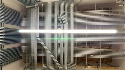 Empty room with exposed wiring, metal shelving, and a bright fluorescent light across the center