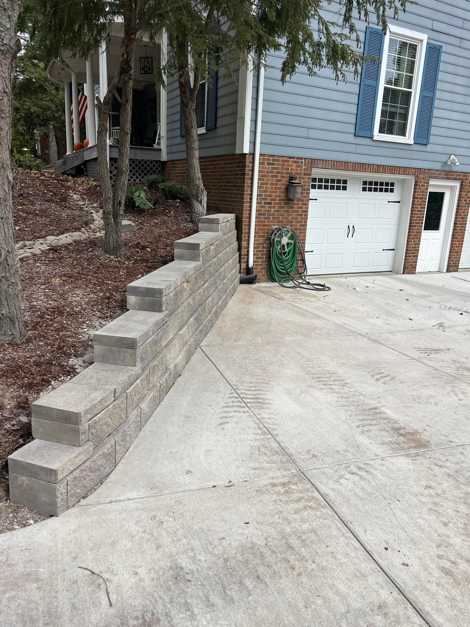 A concrete block retaining wall alongside a driveway leading to a two-car garage and house with blue siding.