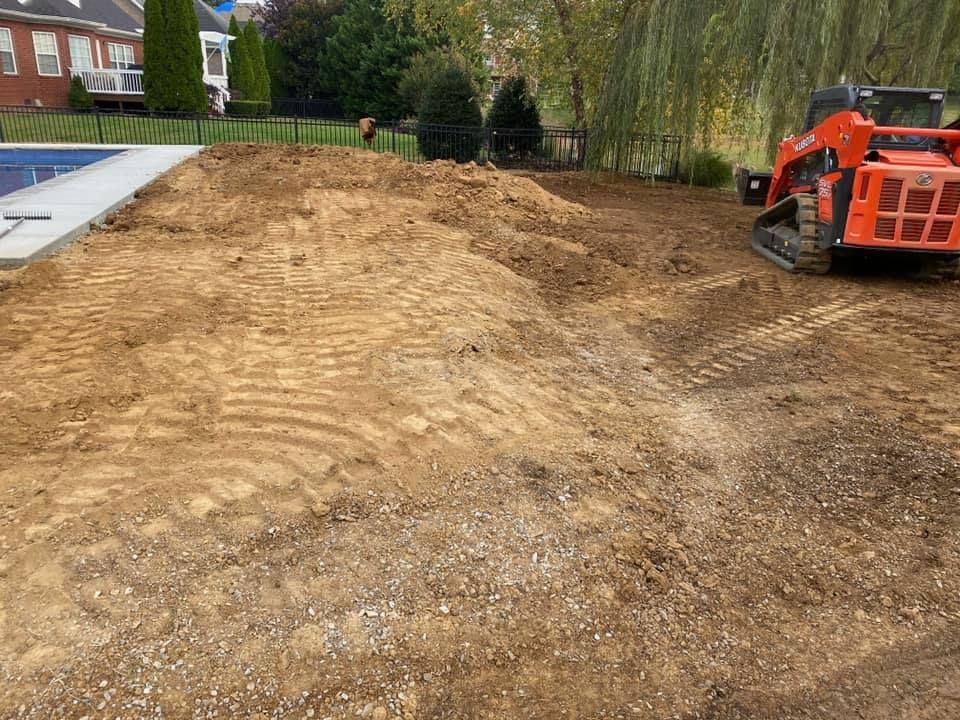 A small orange skid steer on dirt ground. Construction or landscaping with a pool and house in the background.