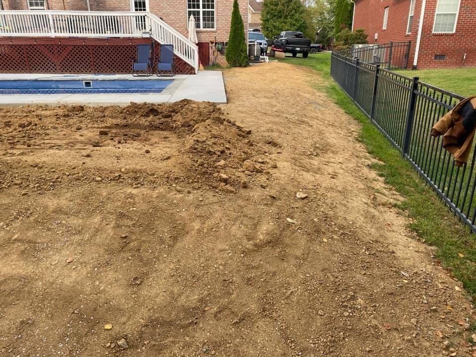 A backyard with a freshly graded dirt area beside a pool and a black fence, with a house in the background.