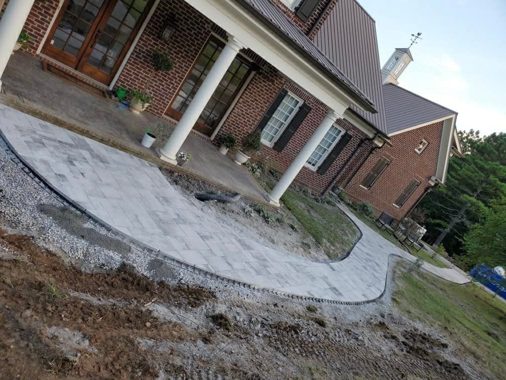 Brick home with a curved stone walkway under construction. Dirt surrounds the walkway, with landscaping being done.