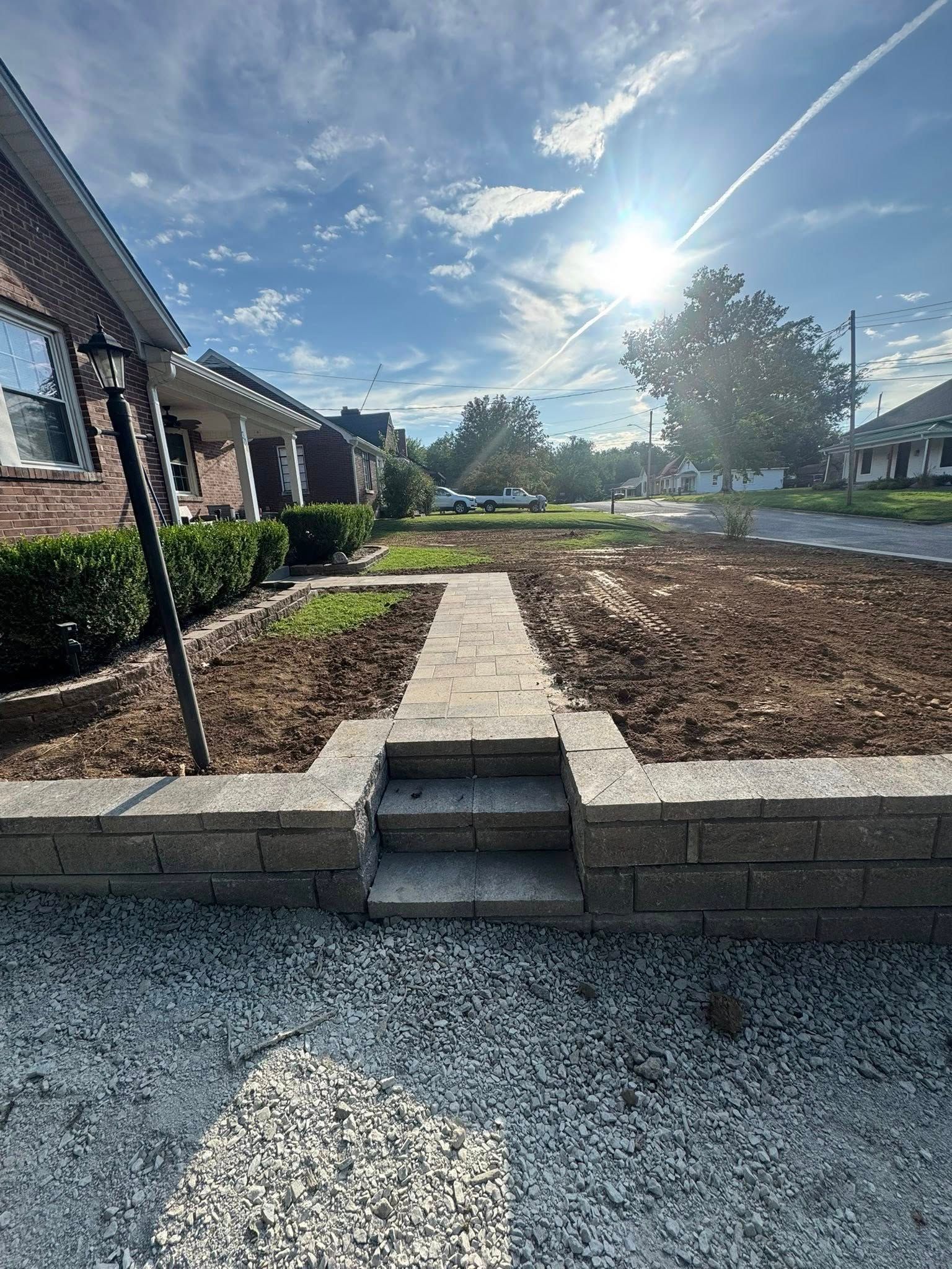 Stone retaining wall with steps leading to a stone pathway through a mulch-covered garden bed, residential setting.
