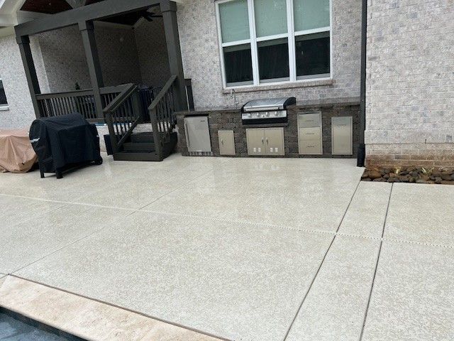 Outdoor kitchen on a concrete patio next to a house with a covered porch.