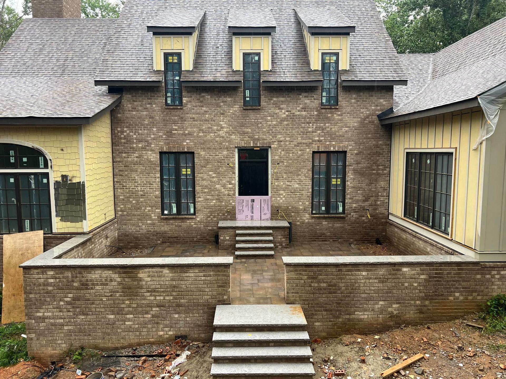 Brick house under construction with multiple windows and a gray roof.