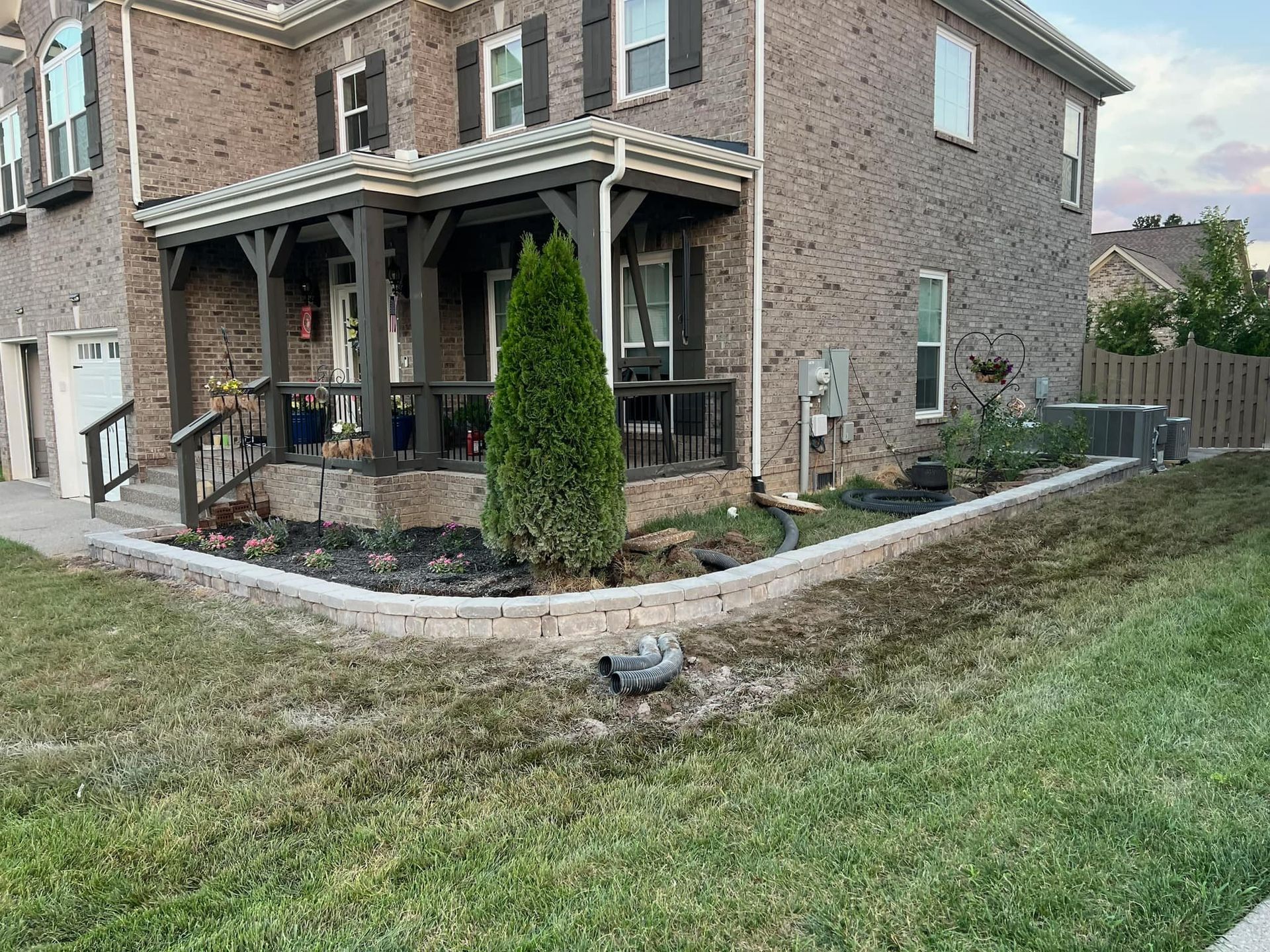 Brick house with a porch and landscaping. A raised garden bed in front has a small tree.