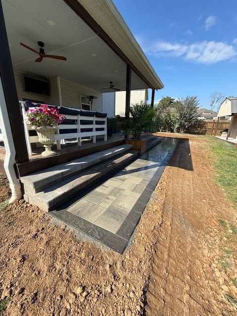 Outdoor patio with paved steps, leading to a covered seating area, brown trim, blue sky, and green grass.