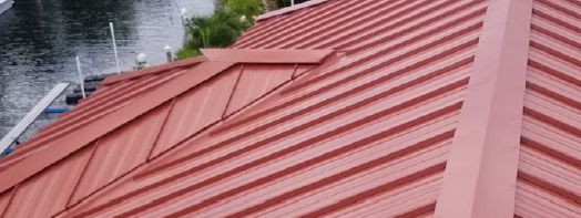 Red metal roof on a building, angled view. Ridged panels.