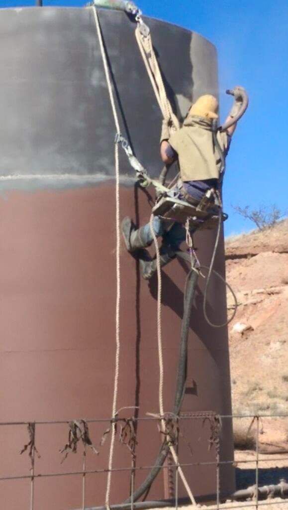 A man is painting a large brown tank with a hose