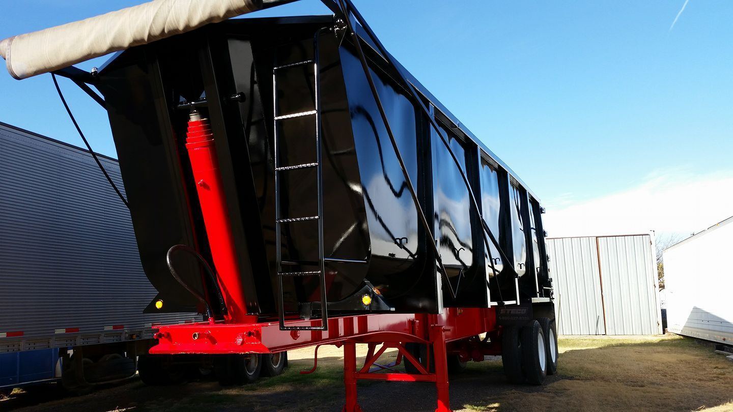 A black and red dump trailer is parked in front of a building.