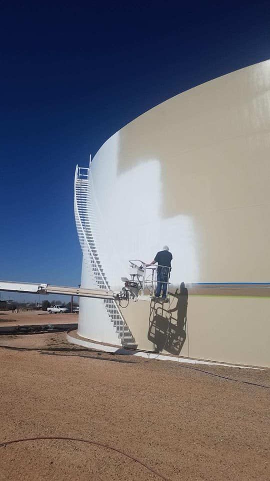 A man is painting the side of a large oil tank.