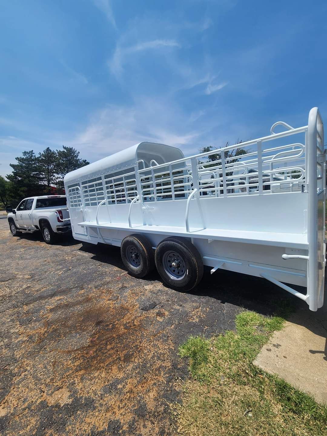 A white horse trailer is parked next to a white truck in a parking lot.