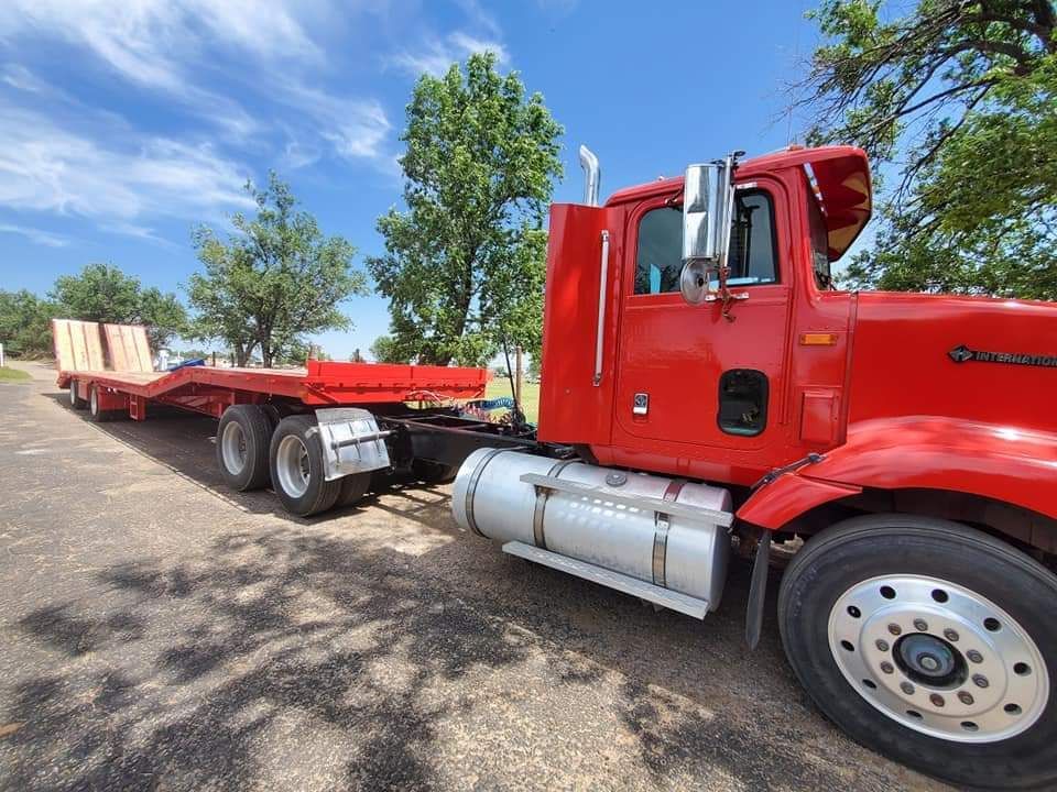 A red semi truck with a flatbed trailer is parked in a parking lot.