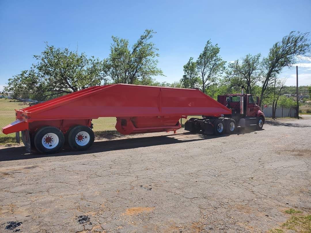 A red truck with a ramp attached to it is parked in a gravel lot.