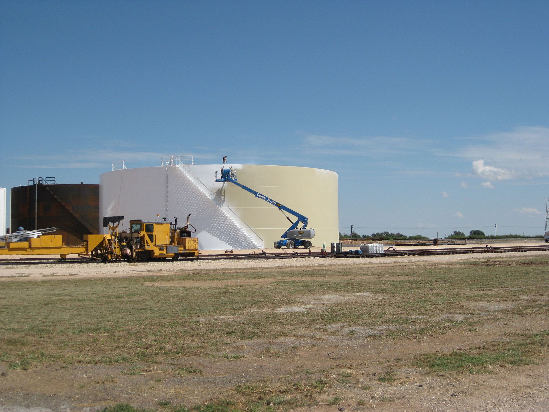 A large tank is being painted in a field