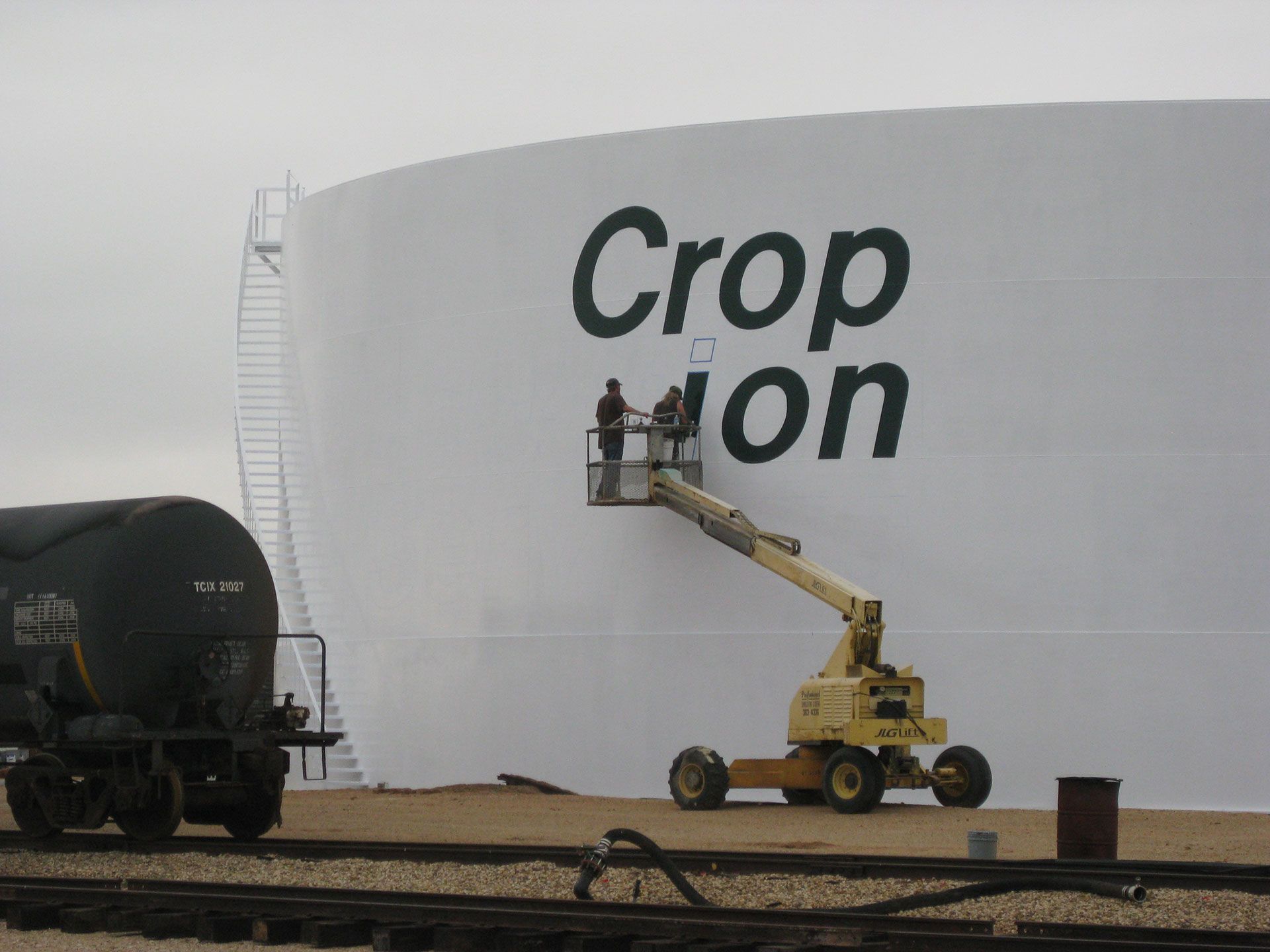 A large white tank with painters working on it