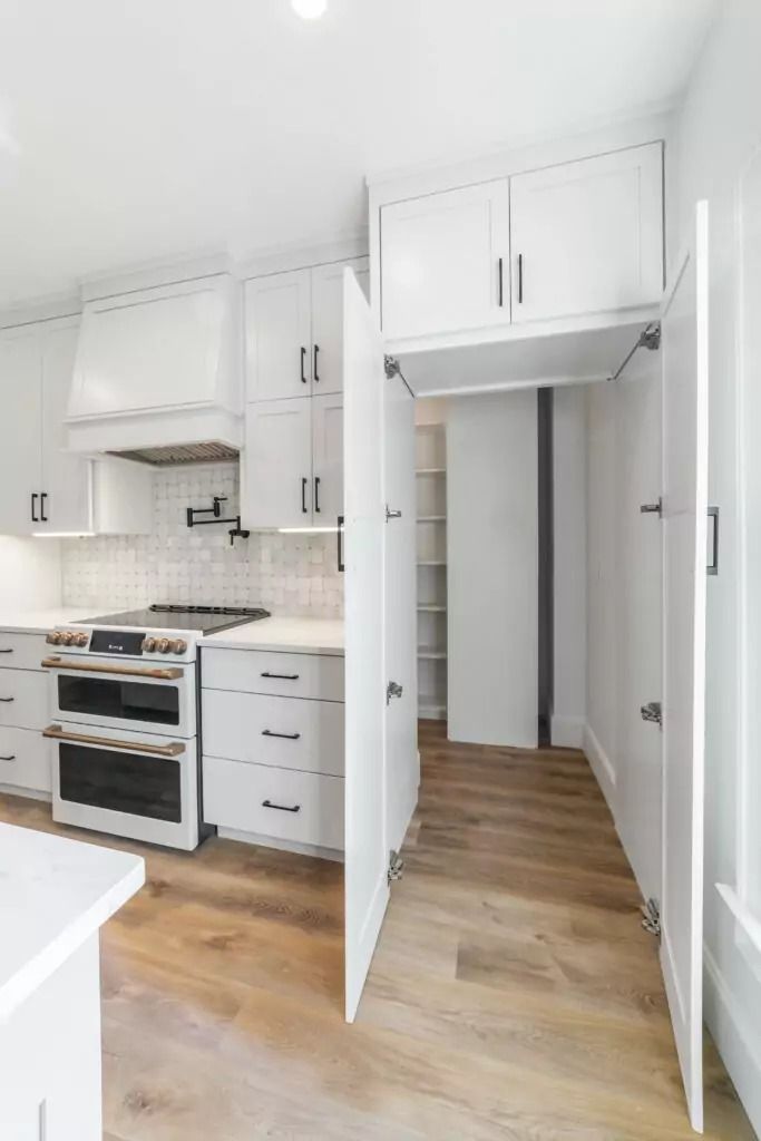 A kitchen with white cabinets , a stove , and a pantry.