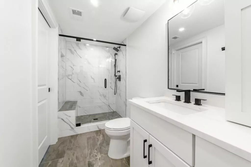A bathroom with a toilet , sink , mirror and walk in shower.