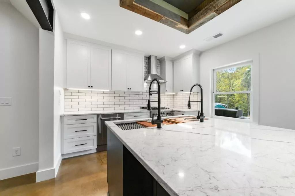 A kitchen with white cabinets , a large island , a sink , and a window.