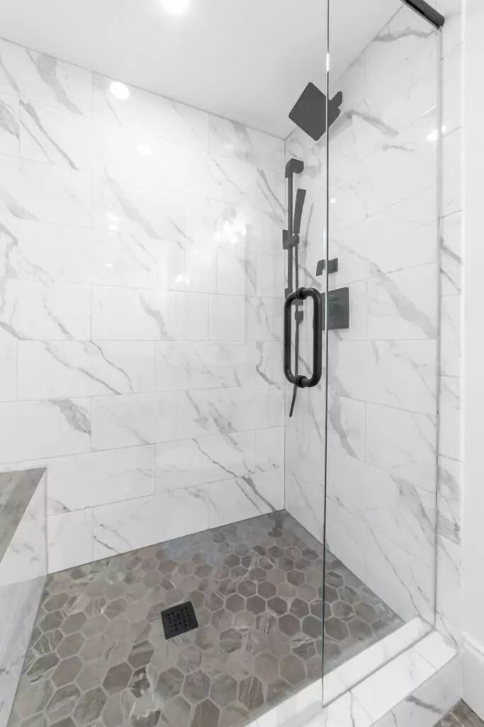 A walk in shower with a glass door and marble walls.