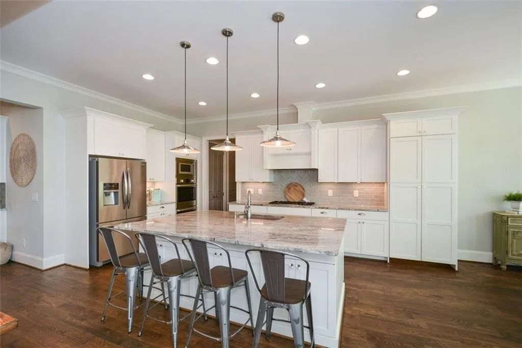 A kitchen with white cabinets , granite counter tops , stainless steel appliances and a large island.