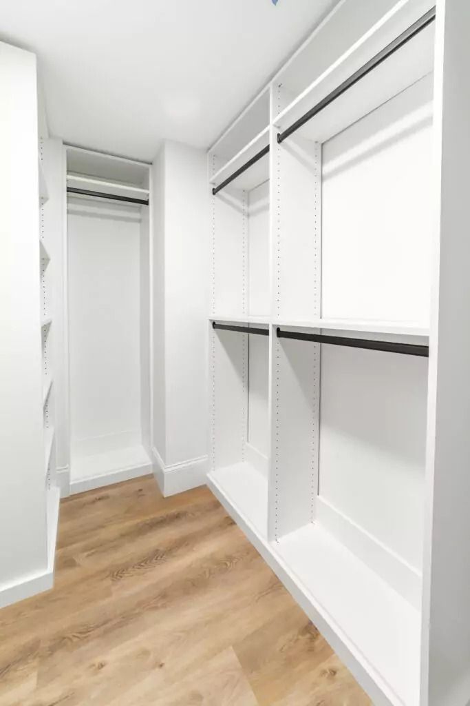 A walk in closet with white shelves and wooden floors.