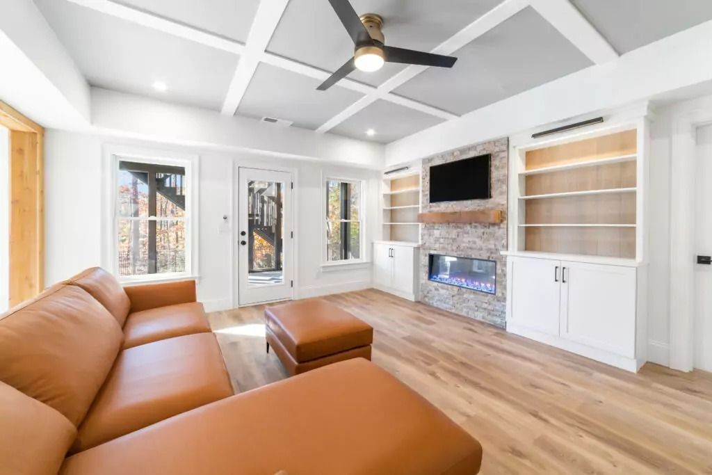 A living room with a brown couch , ottoman , fireplace and ceiling fan.
