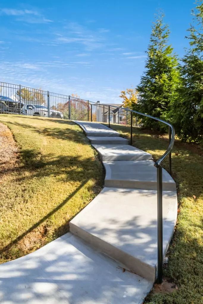 A concrete walkway with a metal railing going up a hill.