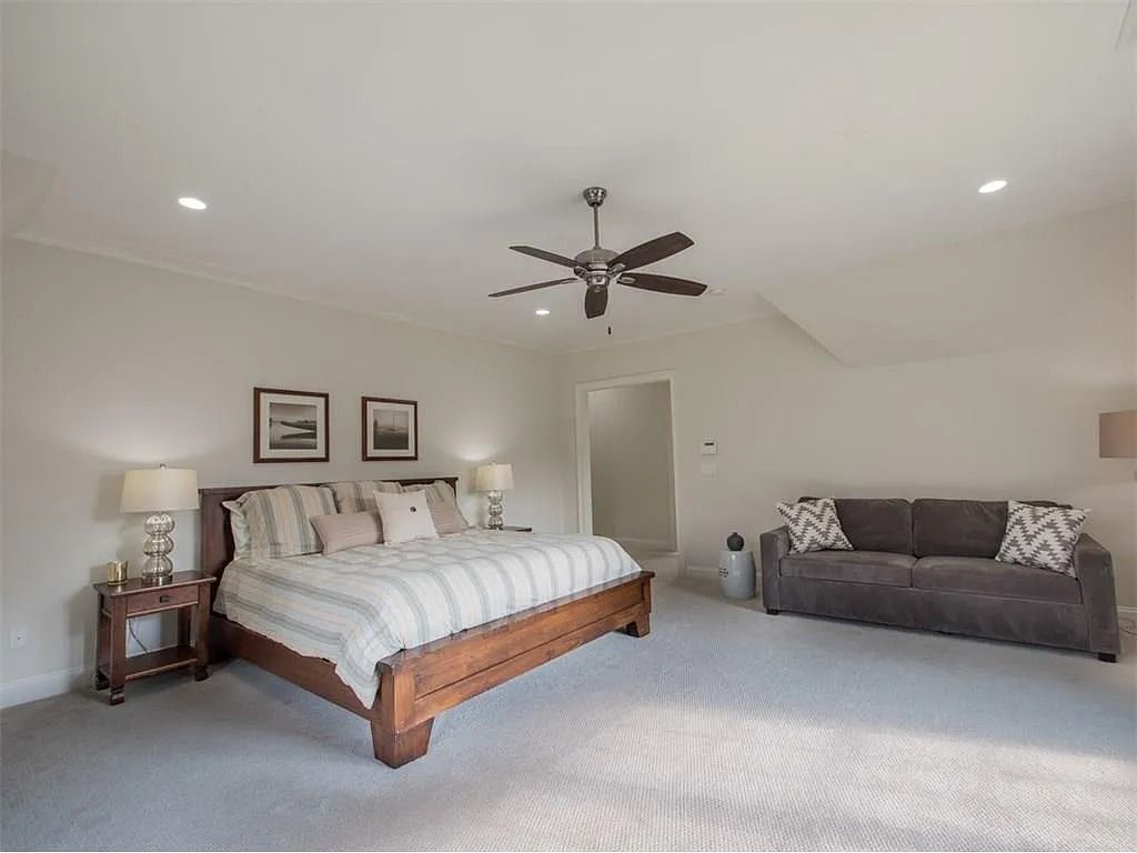 A bedroom with a bed , couch , nightstand and ceiling fan.