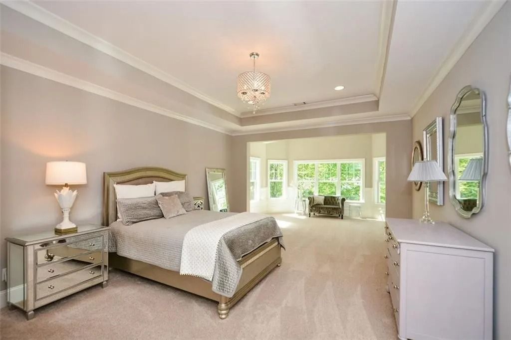 A bedroom with a bed , dresser , nightstand , mirror and chandelier.