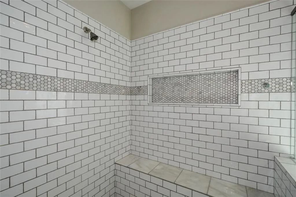 A bathroom with white brick walls and a bench in the shower.