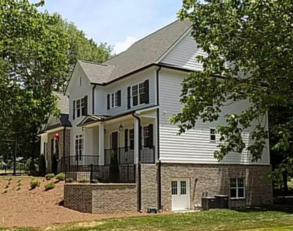 A large white house with black shutters is surrounded by trees.