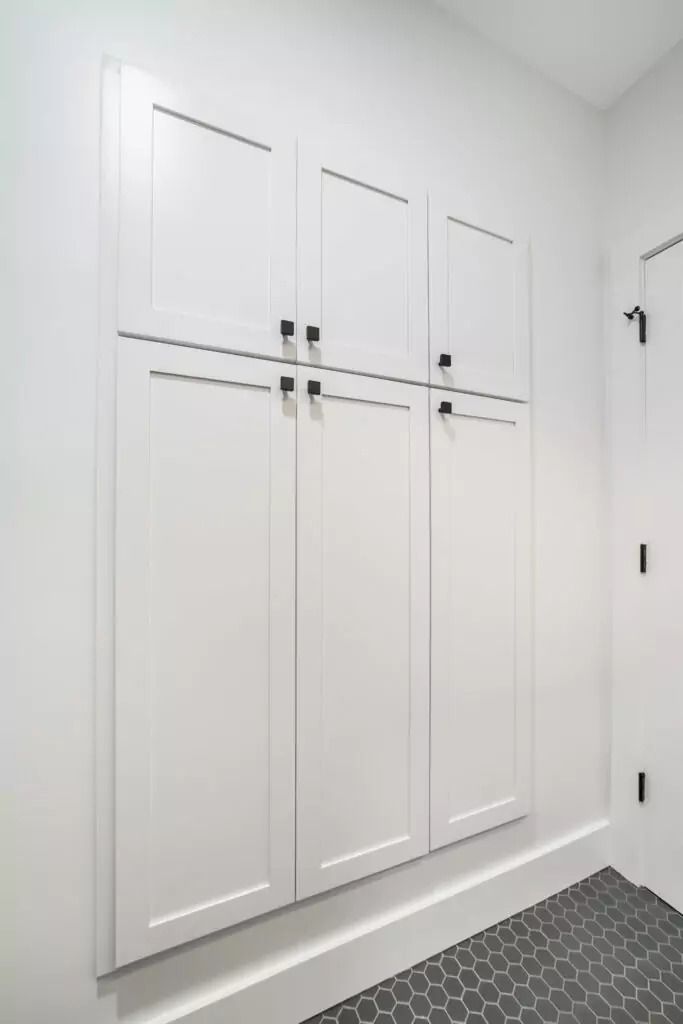 A laundry room with white cabinets and a black tile floor.