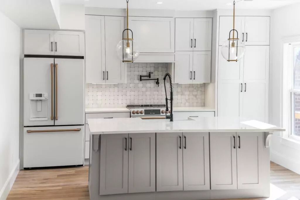 A kitchen with white cabinets , a refrigerator , a sink , and a large island.