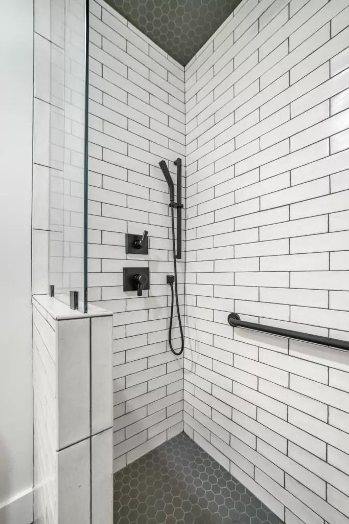 A shower with white tiles and a black handle.