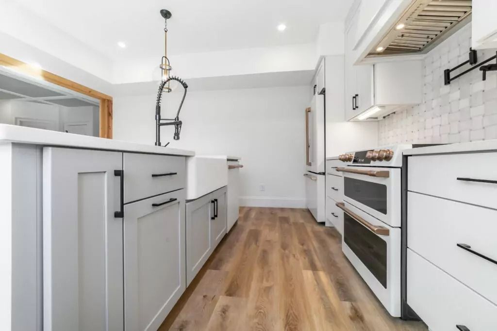 A kitchen with white cabinets , hardwood floors , stainless steel appliances and a sink.