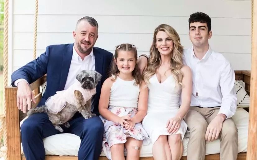 A family is sitting on a porch swing with a dog.