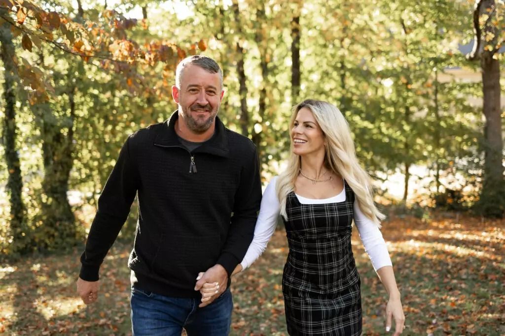 A man and a woman are walking in the woods holding hands.