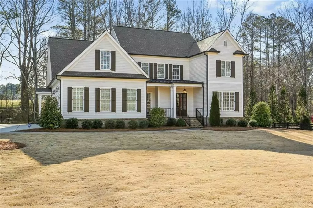A large white house with black shutters is surrounded by trees