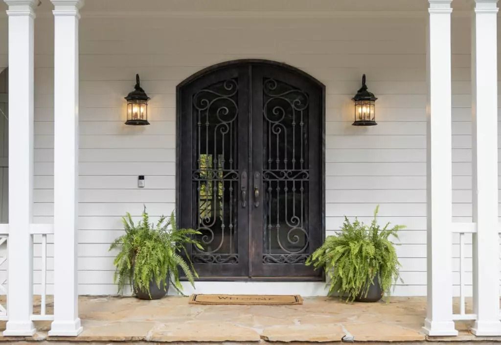 There are two potted plants in front of the door of a house.