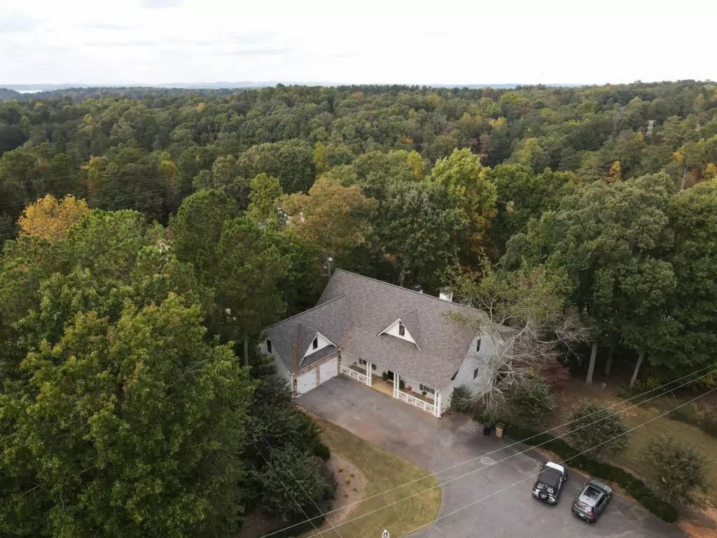 An aerial view of a house in the middle of a forest surrounded by trees.