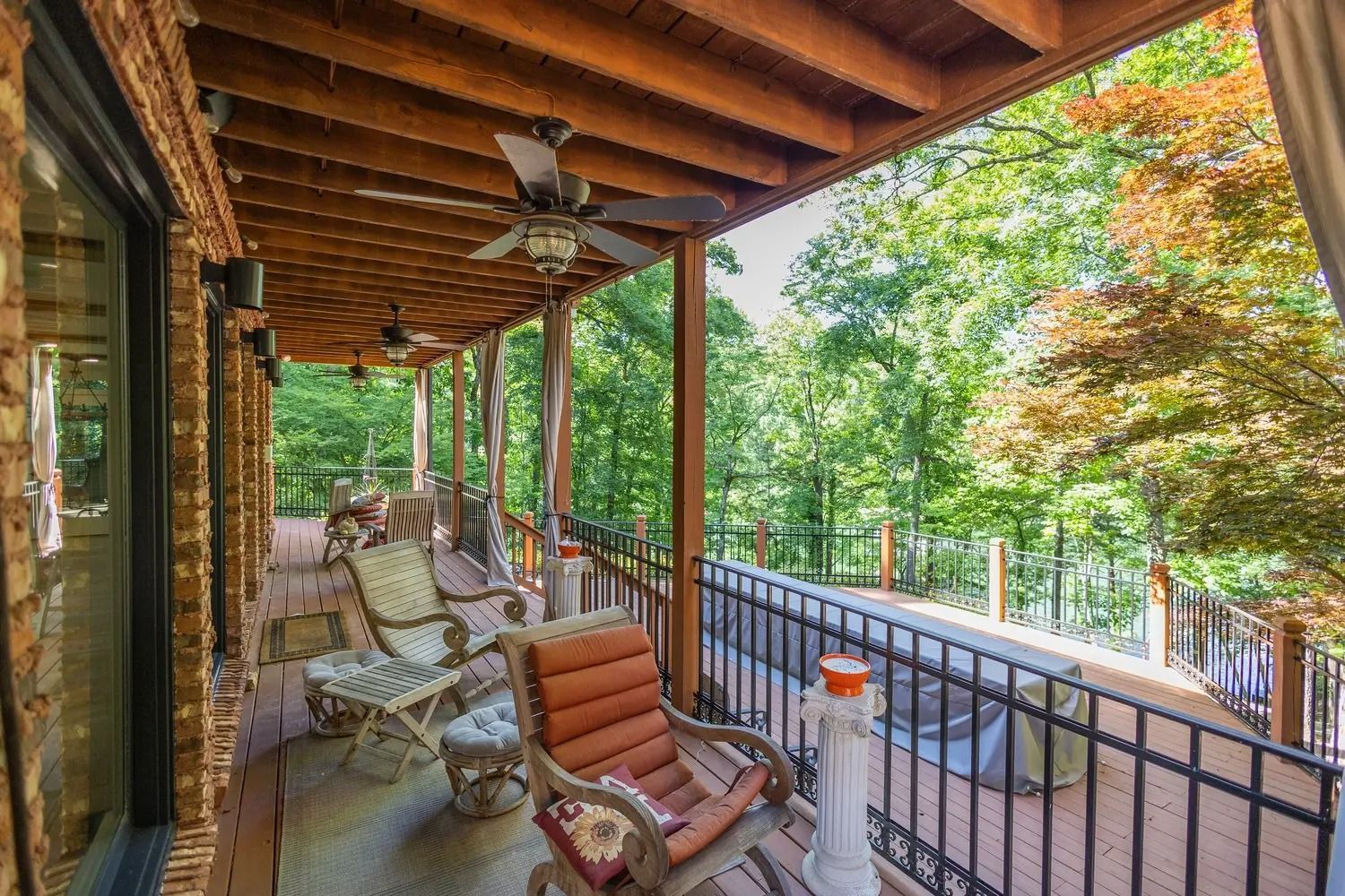 There is a porch with a ceiling fan and chairs on it.